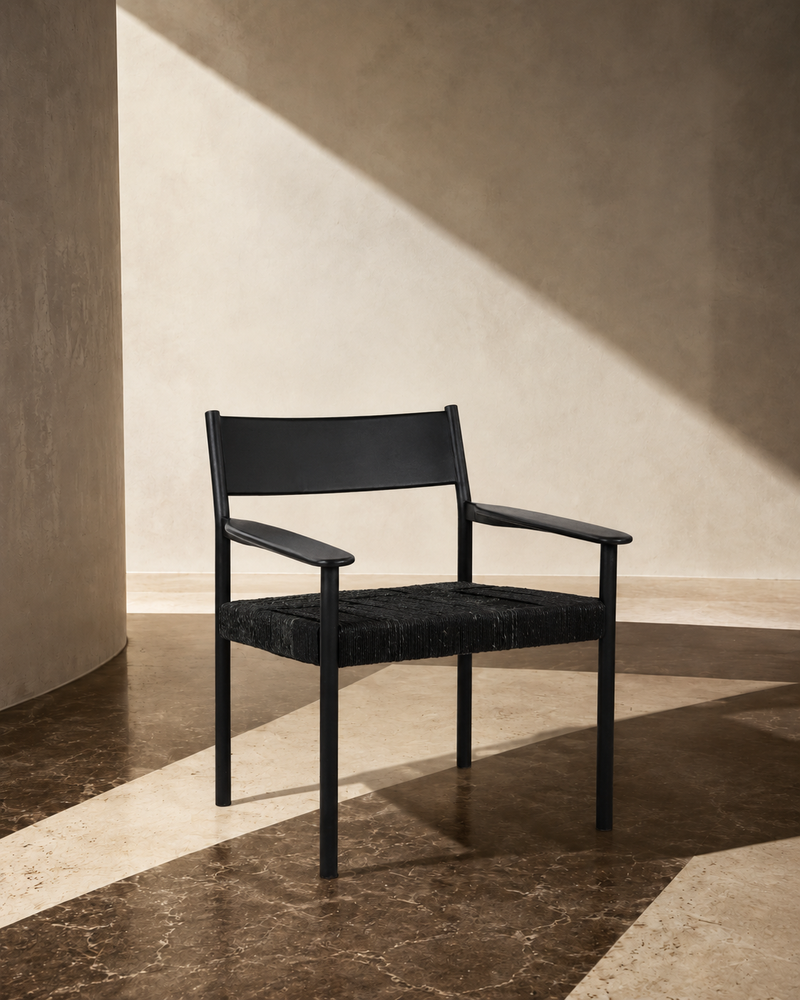 Black lounge chair with solid leather backrest and woven black seat, styled in a sunlit interior