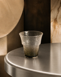 Hand-blown textured glass tumbler with a smoky green-grey gradient base, styled on a metal tabletop