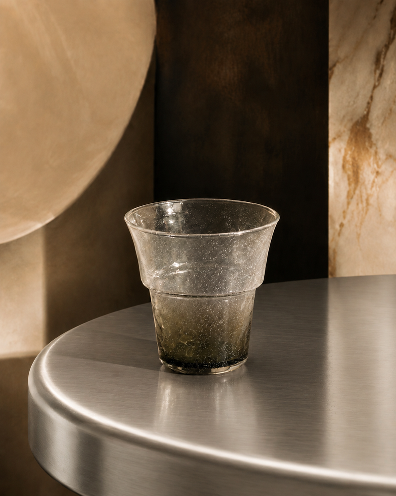 Hand-blown textured glass tumbler with a smoky green-grey gradient base, styled on a metal tabletop