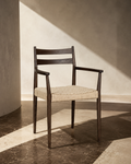Dark oak dining chair with armrests and natural woven cord seat, styled in a sunlit interior