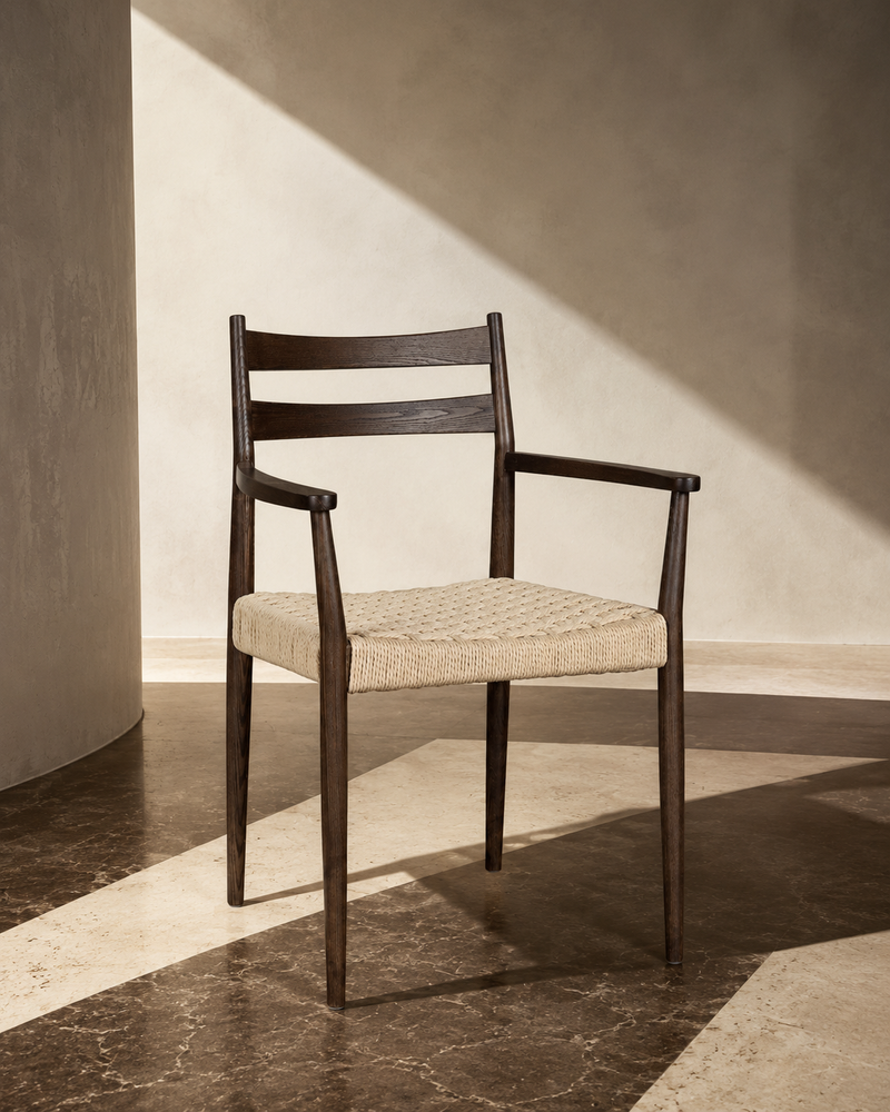 Dark oak dining chair with armrests and natural woven cord seat, styled in a sunlit interior